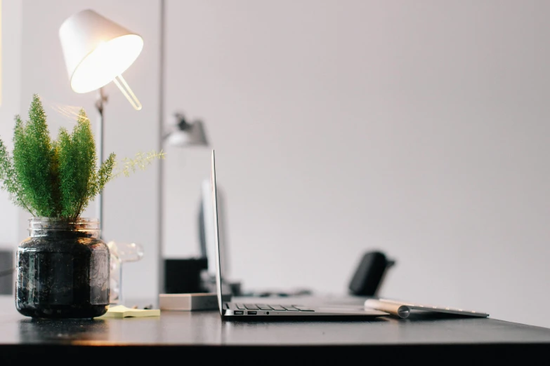 a laptop computer sitting on top of a wooden desk, unsplash, light and space, lamps, well - decorated, lights with bloom, office furniture