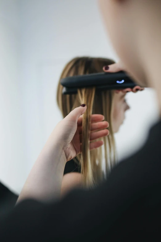 a woman is straightening her hair in front of a mirror, by Adam Marczyński, side view of a gaunt, technologies, designer, close-up photograph