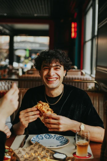 a group of people sitting at a table eating pizza, dark short curly hair smiling, holding his hands up to his face, 2019 trending photo, portrait of a young italian male
