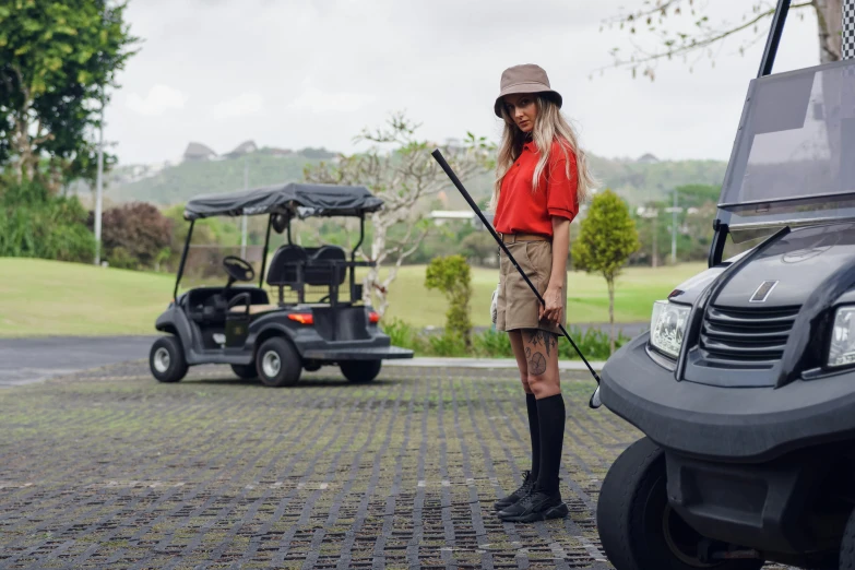 a woman standing next to a golf cart, by Julia Pishtar, unsplash, baggy clothing and hat, avatar image, sweeping, sydney park