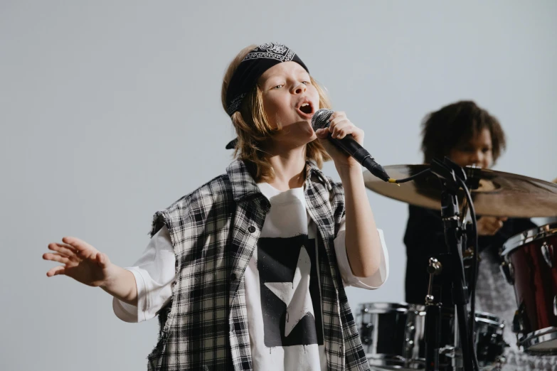 a woman singing into a microphone while standing next to a drum, trending on pexels, greta thunberg, tomboy, studio kyoto, wearing ragged clothing