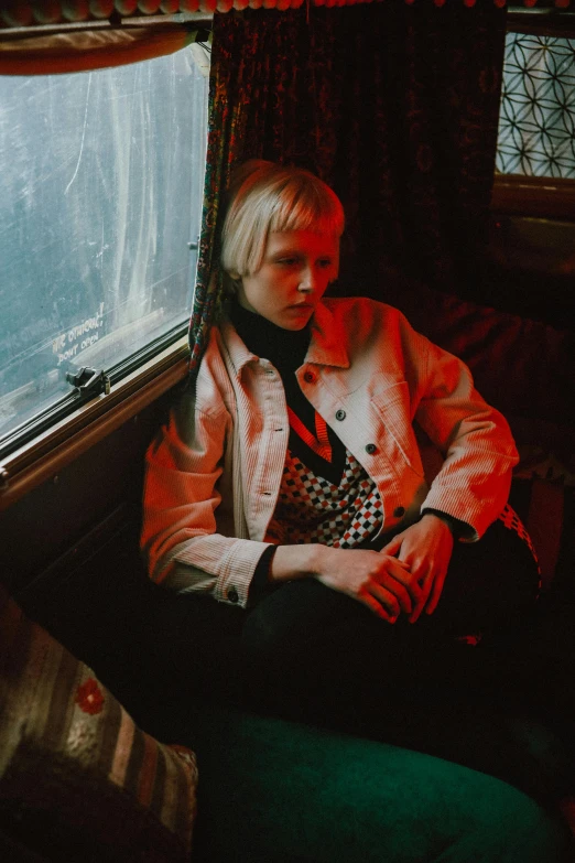 a woman sitting on a train looking out a window, an album cover, unsplash, visual art, short platinum hair tomboy, red jacket, white - blond hair, concert