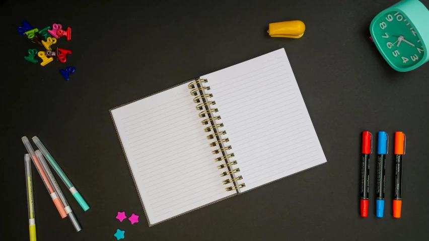 a notepad sitting on top of a desk next to a clock, in front of a black background, confetti, product view, small