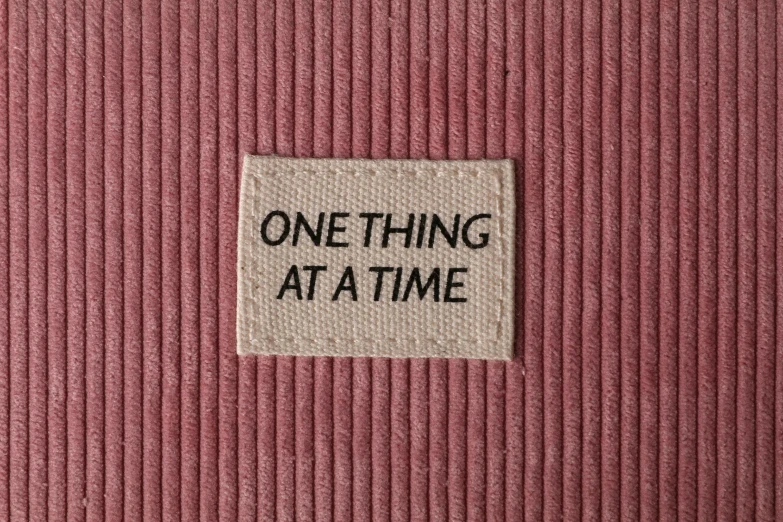 a patch that says one thing at a time, conceptual art, pink, carpet, thumbnail, offwhite