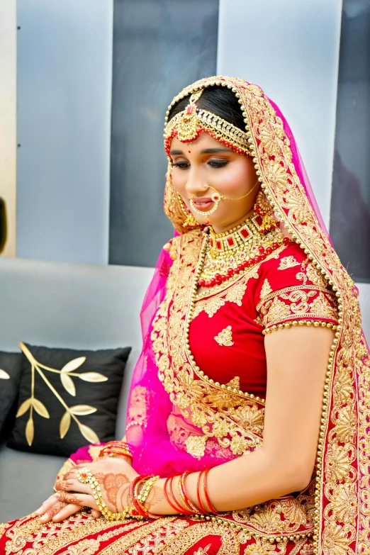 a woman in a red and gold dress sitting on a couch, bride, wearing gold jewellery, profile pic, veil