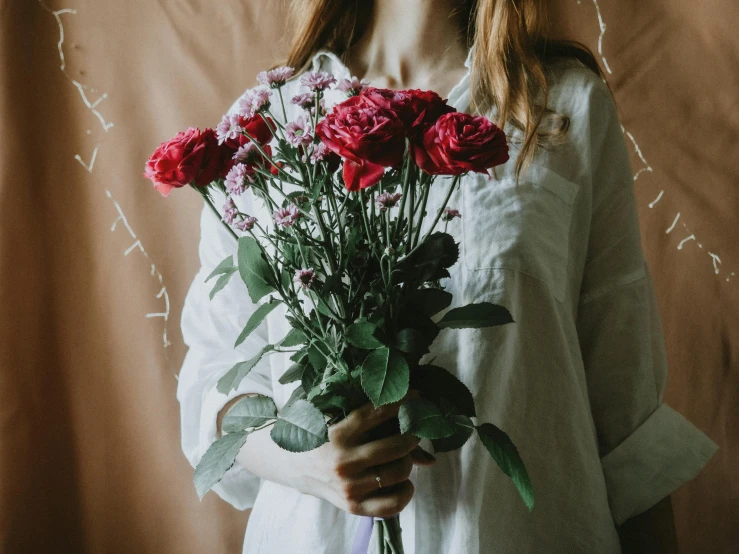 a woman holding a bouquet of red roses, pexels contest winner, wearing a white button up shirt, freckled pale skin, wearing a linen shirt, pink and red color scheme