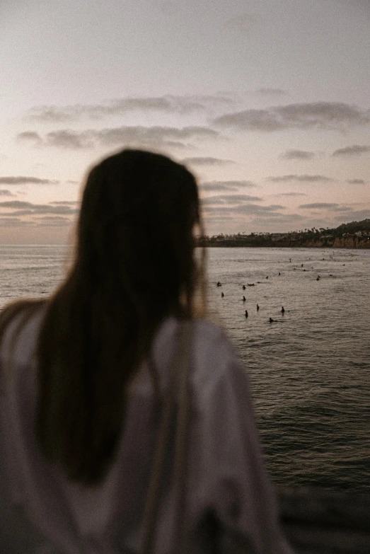 a woman standing in front of a body of water, crowded silhouettes, looking out at the ocean, oceanside, wearing simple robes