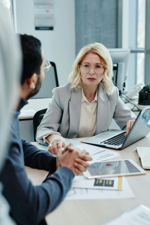 a group of people sitting around a table with laptops, woman in business suit, thumbnail, talking, digital image