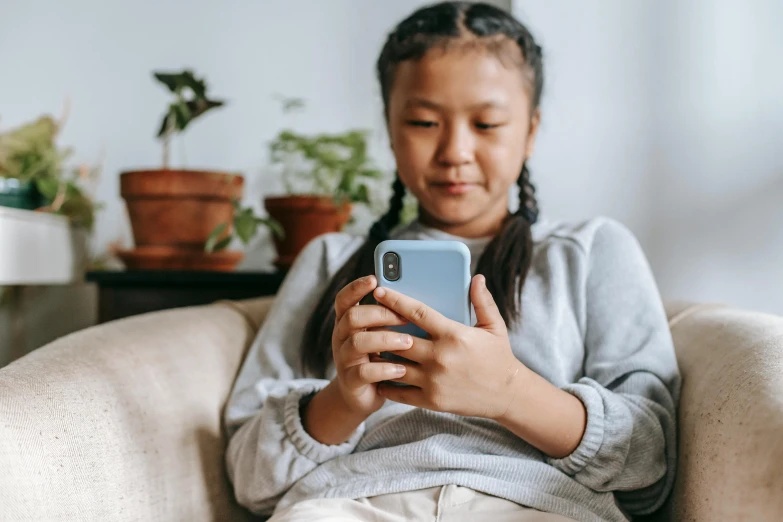 a little girl sitting on a couch using a cell phone, trending on pexels, next to a plant, student, aged 13, rounded corners