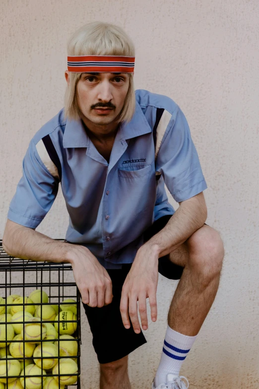 a man sitting next to a basket of tennis balls, an album cover, inspired by Graham Forsythe, trending on reddit, 1990's sears portrait photo, enes dirig, he wears a blue shirt, neo rauch and nadav kander