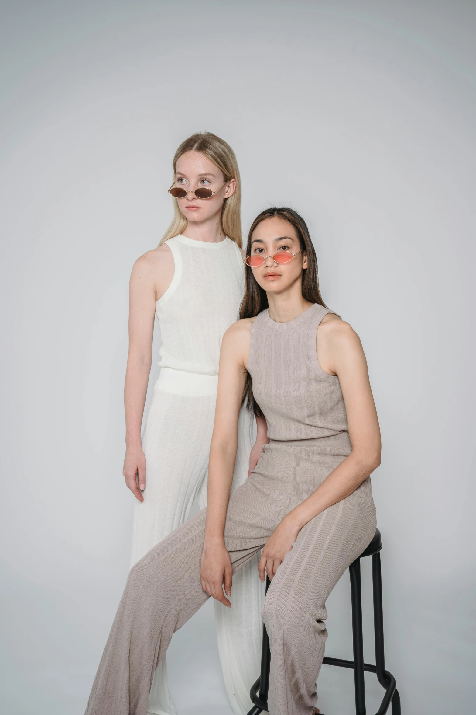 two women sitting next to each other on a stool, trending on unsplash, bauhaus, with square glasses, low quality photo, taupe, off - white collection