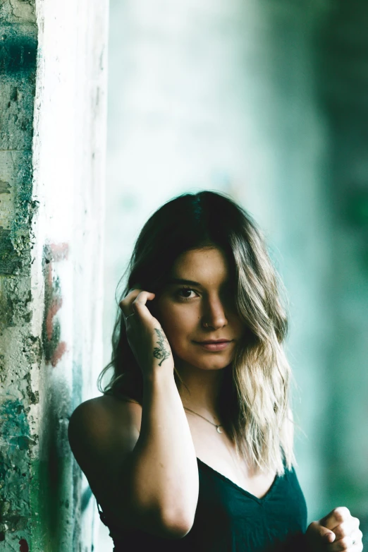 a woman in a black dress leaning against a wall, a colorized photo, inspired by Elsa Bleda, pexels contest winner, concert, halfbody headshot, slightly tanned, vsco film grain