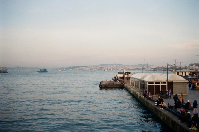 a group of people sitting on top of a pier next to a body of water, inspired by Elsa Bleda, hurufiyya, istanbul, medium format, fish market stalls, hziulquoigmnzhah