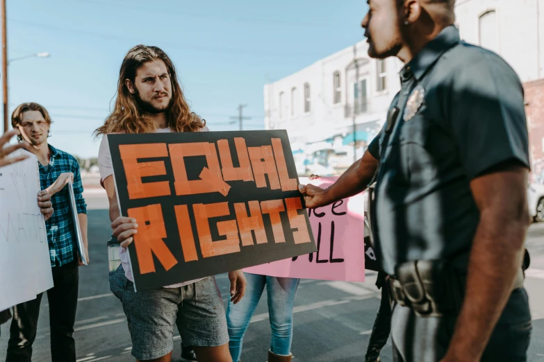 a group of people standing on a street holding signs, trending on pexels, feminist art, two men, police officers, background image, high gradient