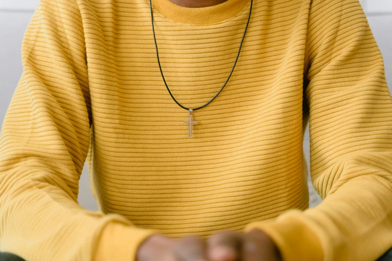 a man sitting in front of a laptop computer, by Nina Hamnett, trending on pexels, hurufiyya, beads cross onbare chest, wearing a yellow hoodie, ankh pendant, wearing stripe shirt