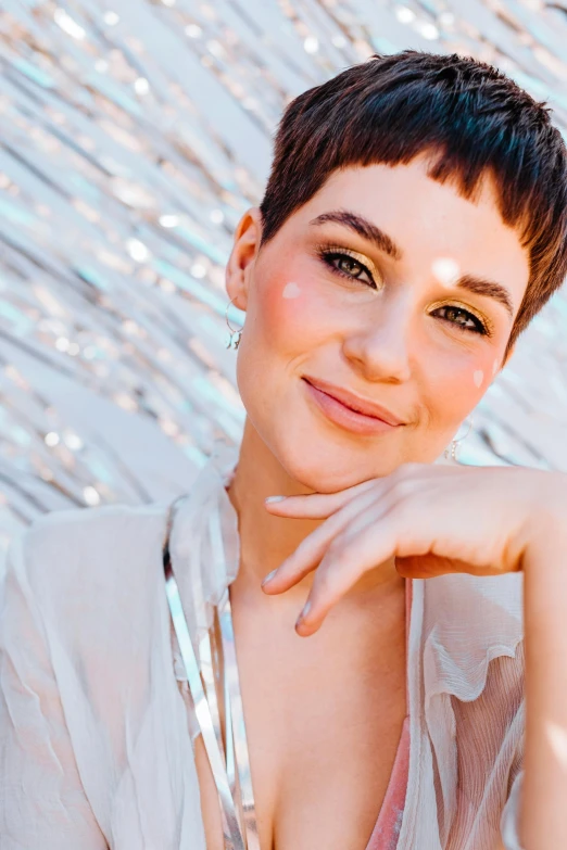 a woman posing for a picture in front of a wall, an album cover, by Julia Pishtar, trending on pexels, pixie cut, with lots of glittering light, ana de la reguera portrait, close - up studio photo