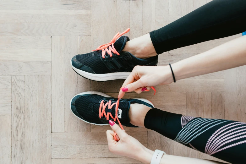 a person tying a pair of shoes on a wooden floor, by Emma Andijewska, pexels contest winner, wearing fitness gear, walking to the right, laces and ribbons, pacing