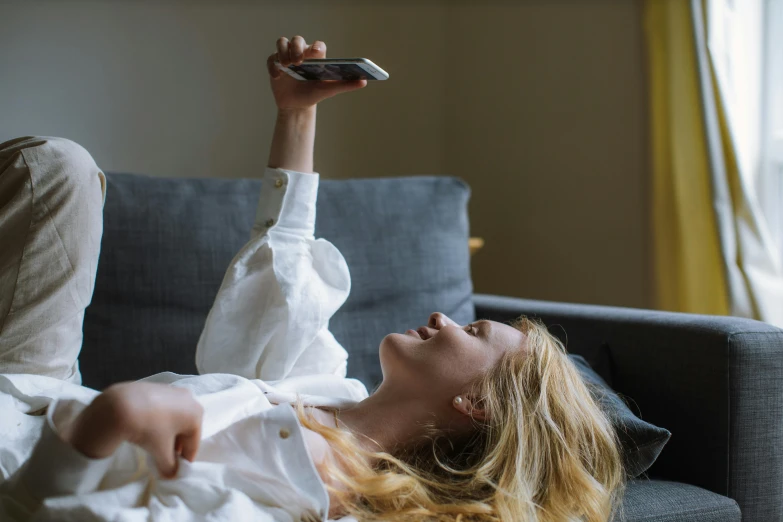 a woman laying on a couch with a remote in her hand, trending on pexels, happening, hold up smartphone, 6 : 3 0 am, sydney sweeney, profile pic