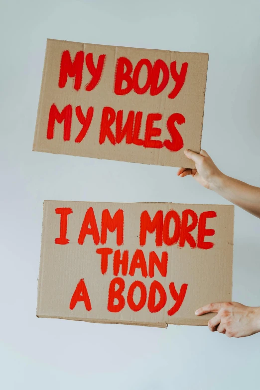two people holding signs that say, my body my rules i am more than a body, a poster, trending on pexels, contracept, human shape, organs, cardboard