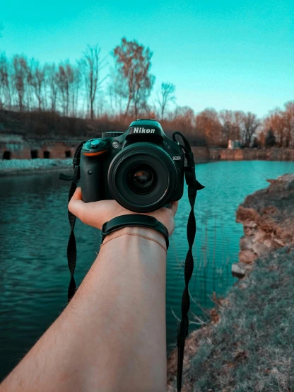 a person holding a camera near a body of water, teal aesthetic, nikon d 7 8 0, instagram post, nikon d 4 x