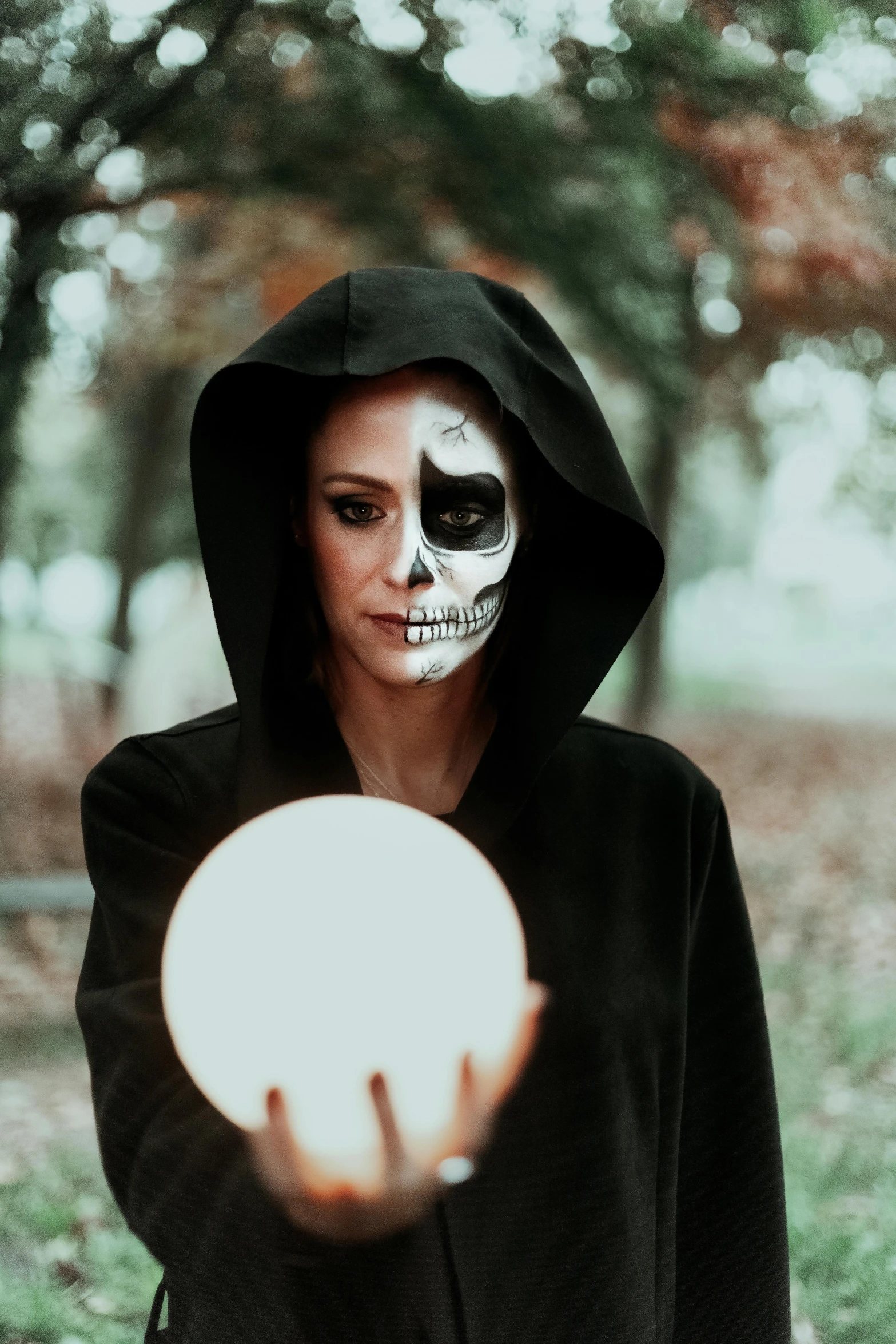 a woman dressed as a skeleton holding a frisbee, by Julia Pishtar, pexels contest winner, holding a crystal ball, wearing a dark hood, black dress : : symmetrical face, the moon cast on the man