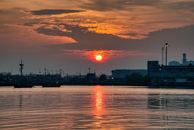 a large body of water with a sunset in the background, by Jan Tengnagel, pexels contest winner, sōsaku hanga, industrial setting, south jakarta, red sun in the background, ad image