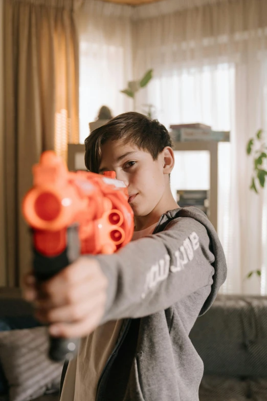 a boy holding a water gun in a living room, pexels contest winner, red airsoft electric pistol, handling riffle on chest, teenage boy, headshot profile picture