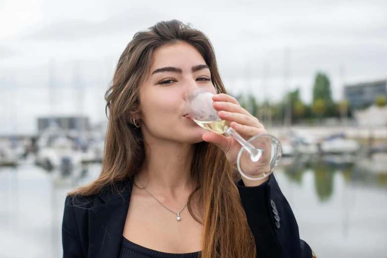 a woman drinking a glass of wine next to a body of water, profile image, harbour, drinking cough syrup, 1 9 year old