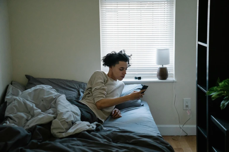 a woman sitting on a bed looking at her cell phone, trending on pexels, queer woman, ashteroth, finn wolfhard, early morning