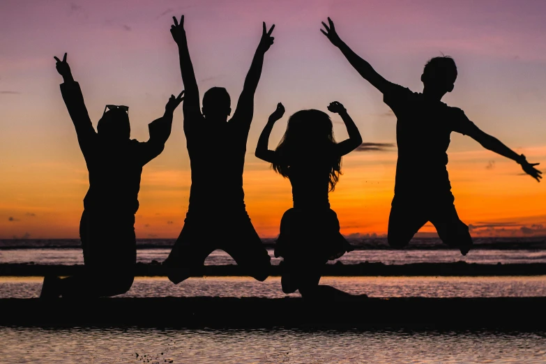 a group of people standing on top of a beach, by Carey Morris, pexels contest winner, jumping for joy, avatar image, silhouette, youth