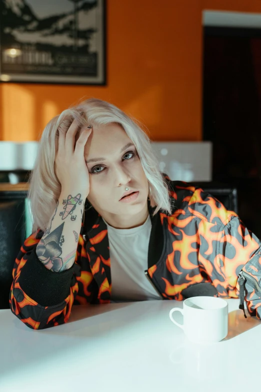 a woman sitting at a table with a cup of coffee, an album cover, inspired by Elsa Bleda, trending on pexels, graffiti, platinum hair, looking confused, androgynous male, hotel room