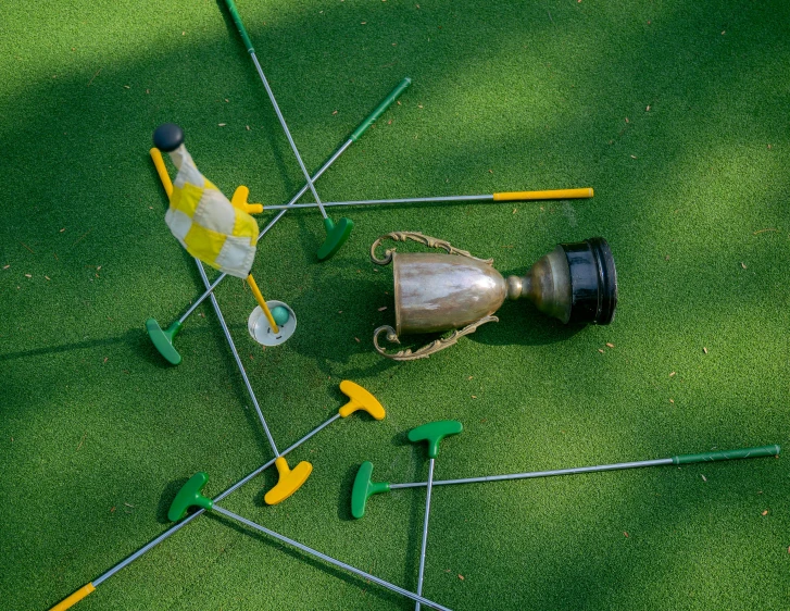 a group of golf clubs sitting on top of a green field, overturned ornate chalice, fake grass, scattered props, birdseye view