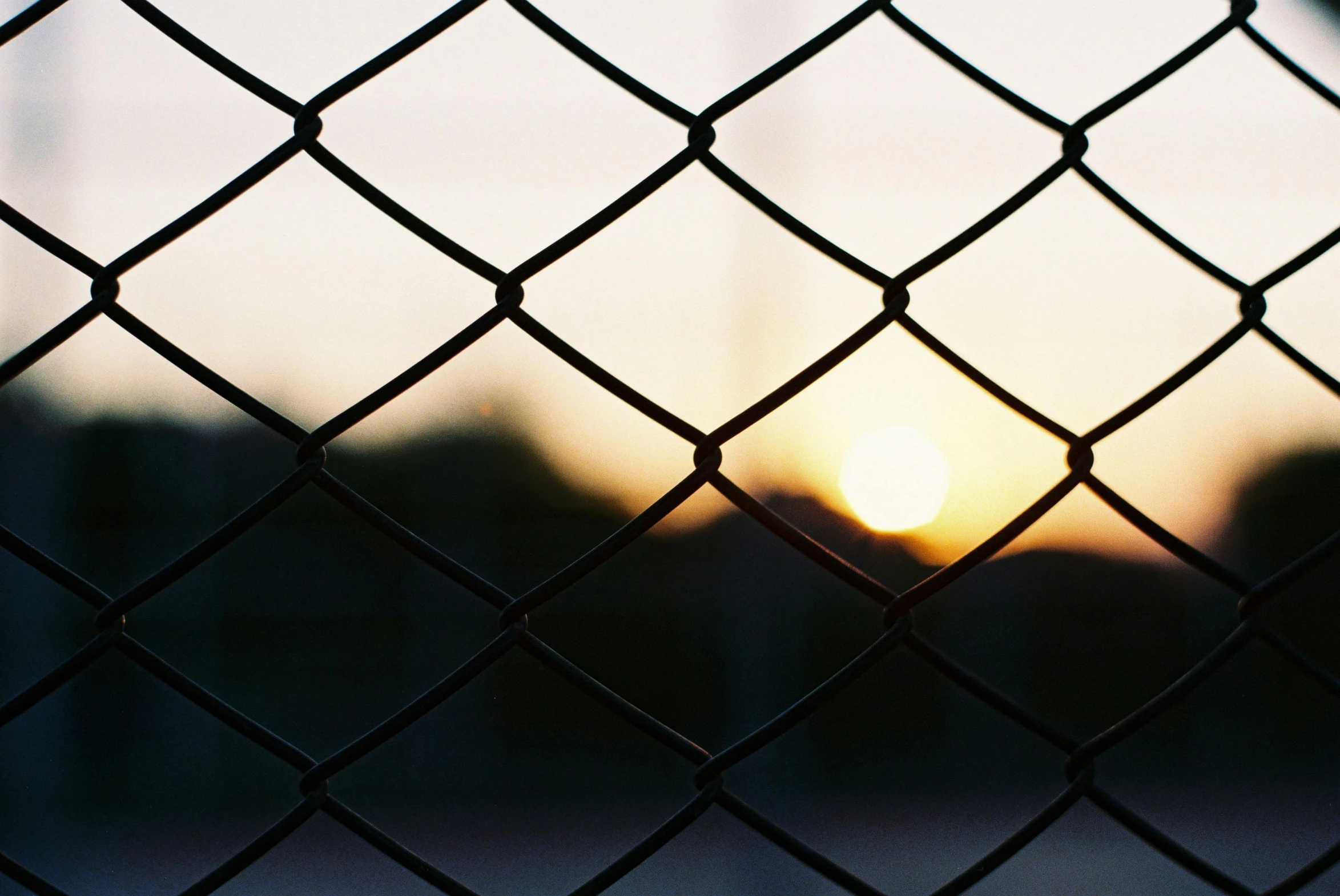 the sun is setting behind a chain link fence, a picture, inspired by Elsa Bleda, unsplash, modernism, videogame still, cage, desktop wallpaper