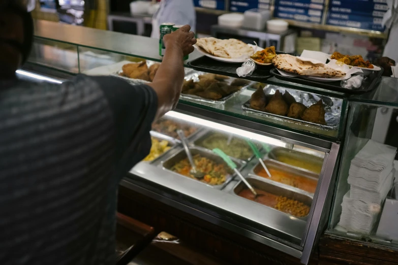 a man standing in front of a display case filled with food, hurufiyya, serving suggestion, hands on counter, avatar image, candid photograph