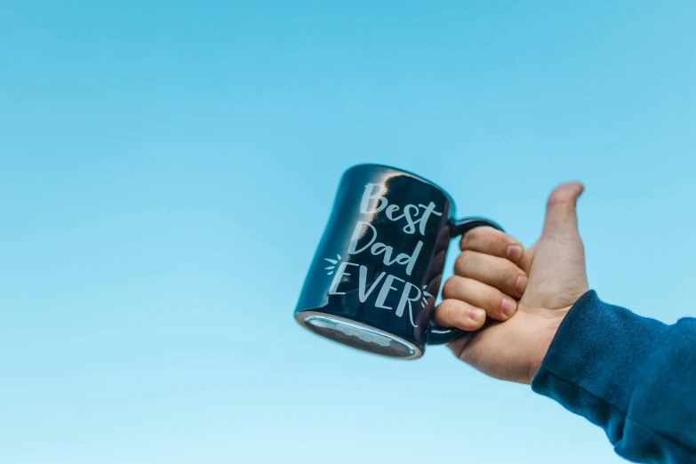 a person holding a coffee mug with the words best dad ever written on it, pexels contest winner, blue skies, press shot, doing a thumb up, black