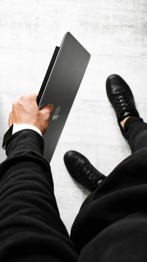 a man in a suit is holding a laptop, by Carey Morris, trending on unsplash, wearing black boots, high angle shot, panel of black, high quality photo
