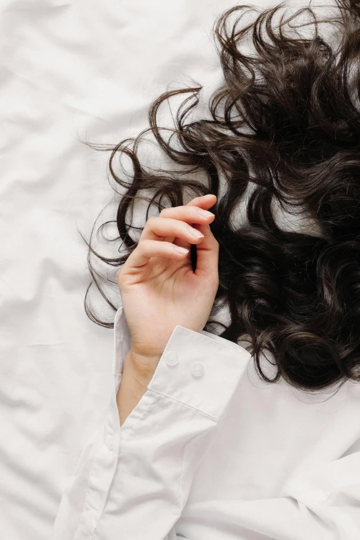a close up of a person laying on a bed, trending on pexels, long wavy dark hair, on white background, curls, hands