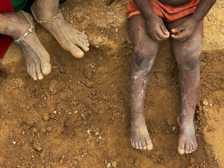 a group of people sitting on top of a dirt field, an album cover, by Robert Jacobsen, pexels contest winner, hurufiyya, looks like varicose veins, muddy colors, aboriginal capirote, photo of poor condition