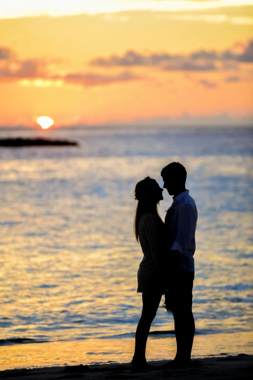 a couple standing next to each other on a beach, during a sunset, on the ocean water, on an island