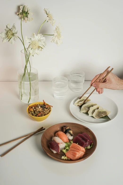 a table topped with plates of food and chopsticks, inspired by Nishida Shun'ei, unsplash, realism, two hands reaching for a fish, soft zen minimalist, japanese related with flowers, sydney hanson