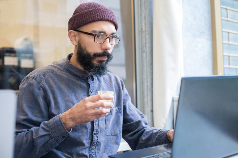 a man sitting at a table using a laptop computer, a portrait, trending on unsplash, aboriginal australian hipster, with a drink, in square-rimmed glasses, ayamin kojima