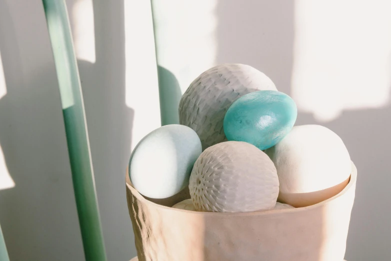 a bucket filled with eggs sitting on top of a table, a marble sculpture, unsplash, soft blues and greens, puffballs, close-up product photo, light cyan