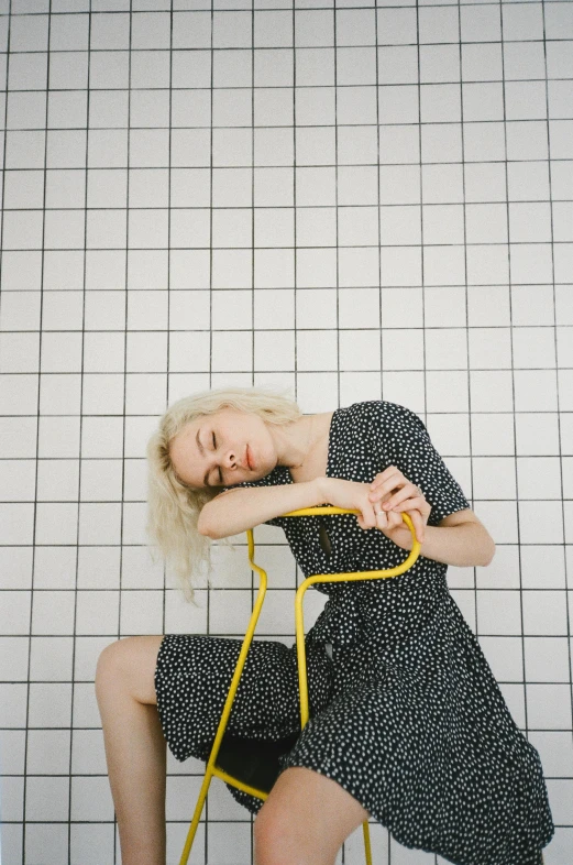 a woman sitting on top of a yellow chair, by Sara Saftleven, unsplash, conceptual art, on a checkered floor, young blonde woman, head tilted downward, polkadots