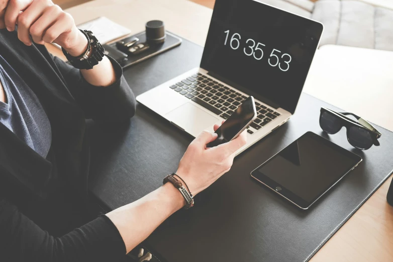 a woman sitting at a table with a laptop and cell phone, trending on pexels, black theme, 9 9 designs, coding time, on a desk