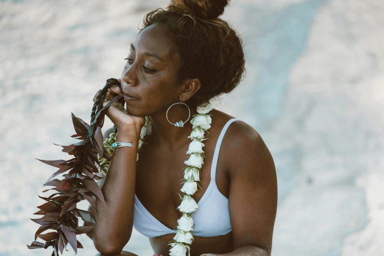 a woman in a white bikini sitting on a rock, trending on unsplash, hurufiyya, flowers on hair, puka shell necklace, dark-skinned, thoughtful expression