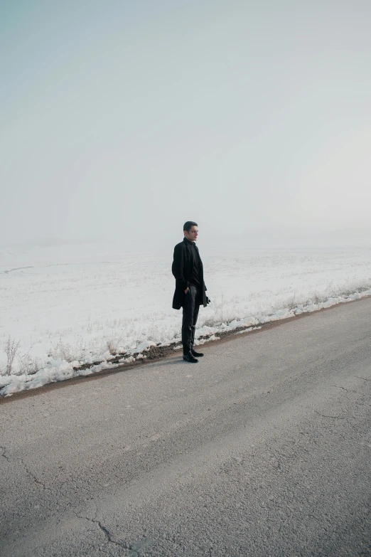 a man standing on the side of a road, an album cover, by Attila Meszlenyi, pexels contest winner, snowy plains, man in black suit, pondering, wide full body