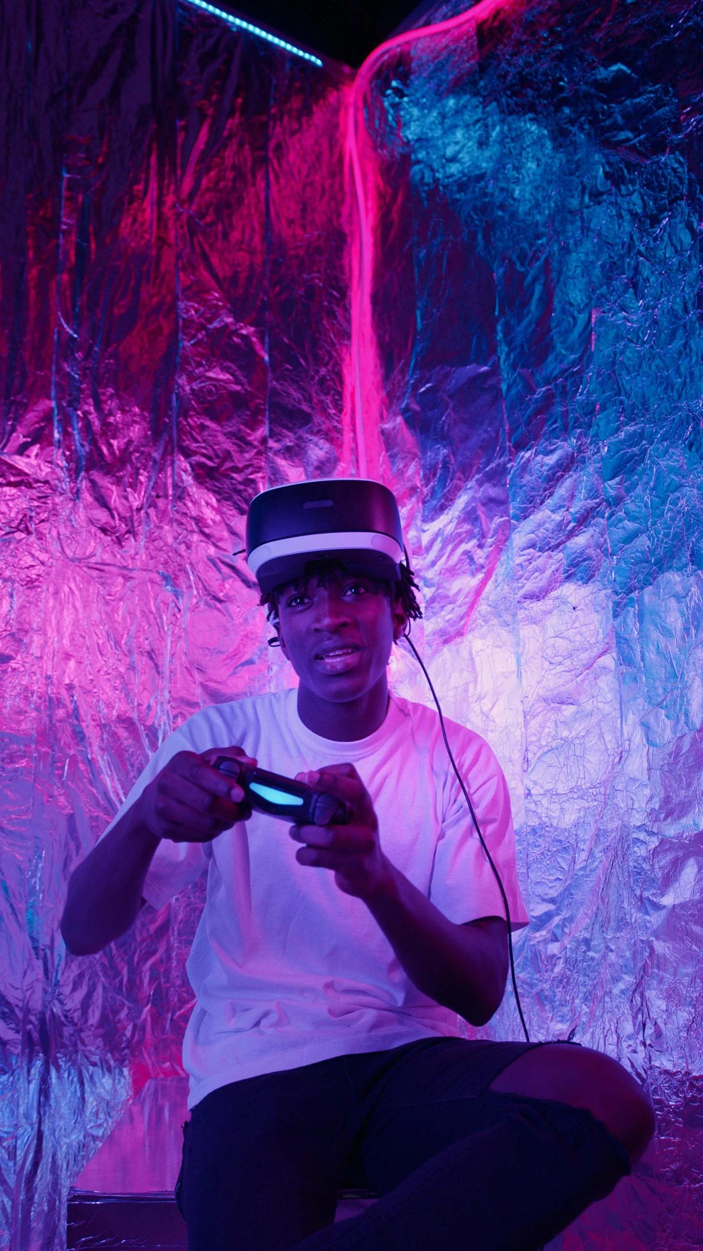 a man sitting on the ground playing a video game, an album cover, by Charles Martin, pexels, afrofuturism, with neon visor, black teenage boy, point of view of visor wearer, indoor shot