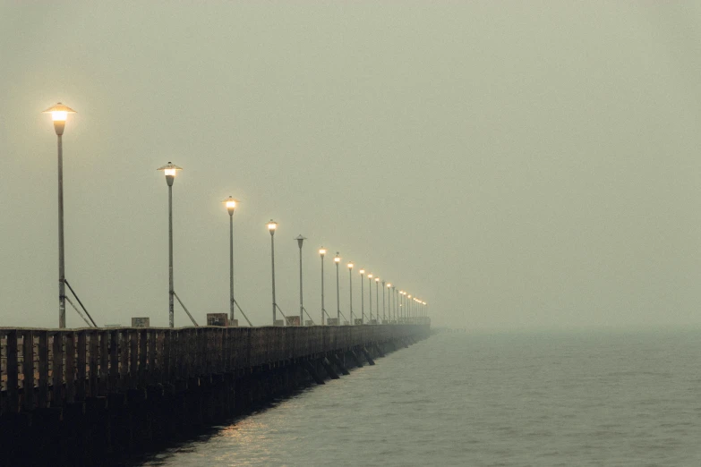 a pier on a foggy day with street lights, inspired by Elsa Bleda, pexels contest winner, smoke billows over the horizon, lamp posts, where a large, damp