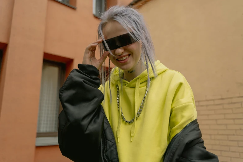 a woman in a yellow and black jacket talking on a cell phone, inspired by Elsa Bleda, trending on pexels, billie eilish portrait, cyber goggles, wearing a grey hooded sweatshirt, avatar image