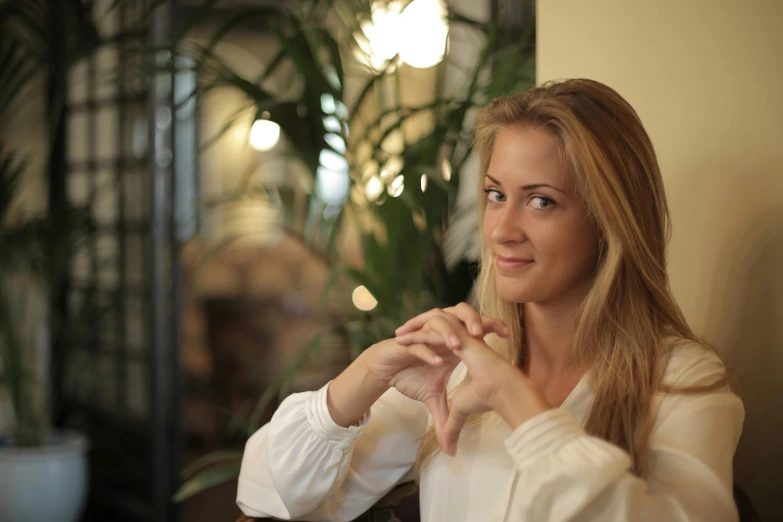 a woman sitting at a table with a glass of wine, with long blond hair, clothed in white shirt, ekaterina, lovingly looking at camera